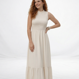 Vestido largo crema sin mangas con cuerpo fruncido, cuello alto y falda larga con volante escalonado, ideal para matrimonios de día, grados y eventos especiales